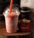 Delicious strawberry milkshake in a disposable cup with straw on a wooden board.